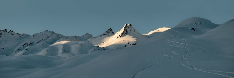 A snow-covered mountain range with a prominent peak and ski tracks.