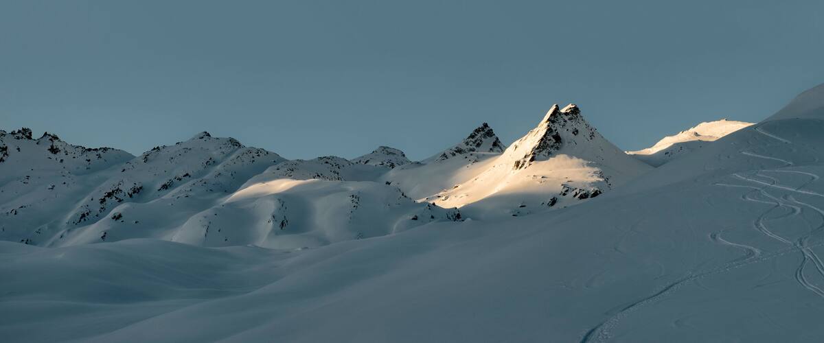 A snow-covered mountain range with a prominent peak and ski tracks.