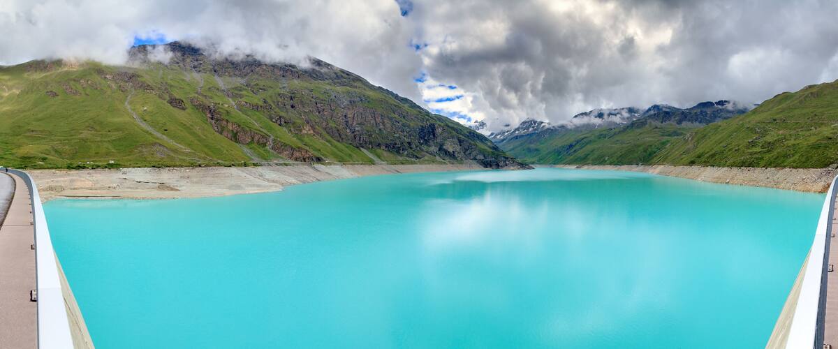 A turquoise lake surrounded by mountains under a cloudy sky.