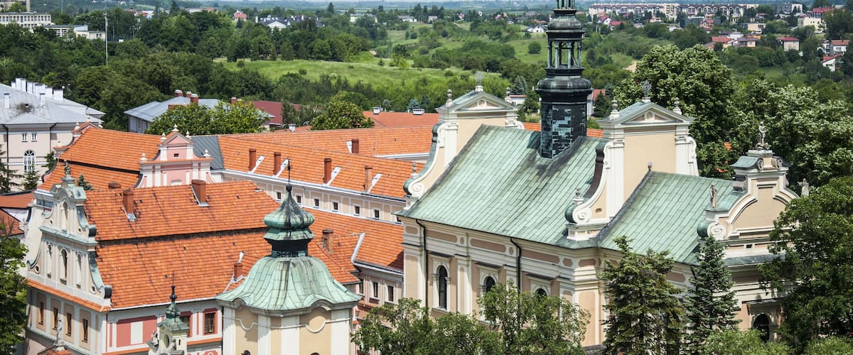 A cityscape with historic buildings, a prominent church with a green roof, and a distant view of a river.