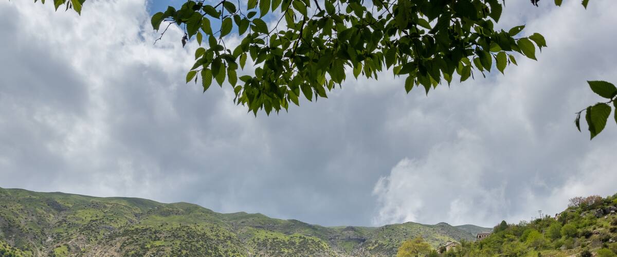 A village nestled in a valley with green hills and a cloudy sky.