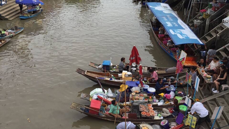 A bustling floating market with numerous boats docked along a narrow waterway, surrounded by buildings and vendors selling goods.