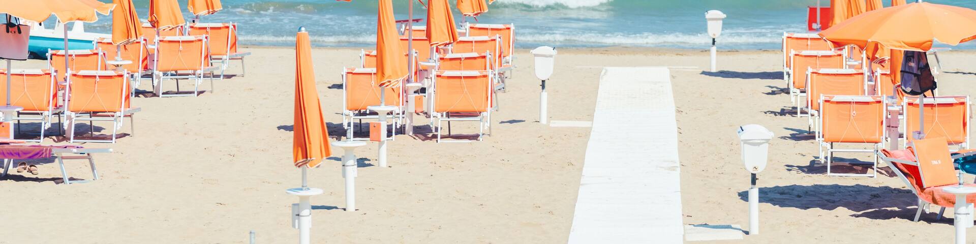 Sunbeds and parasols on the seashore. Beach, sea and umbrellas on summer day. Adriatic coast, Rimini, Italy, view from Gabicce Mare.