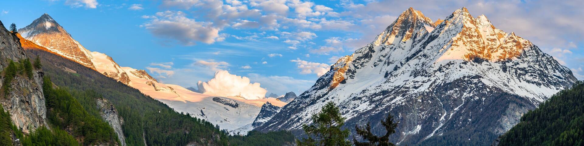 Alpine mountain landscape above Val Herens in Switzerland at sunset with peaks covered by snow and a very big cloud