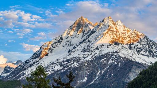 Alpine mountain landscape above Val Herens in Switzerland at sunset with peaks covered by snow and a very big cloud