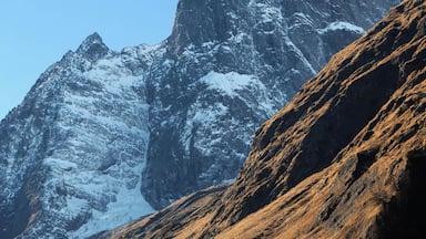 A snow-covered mountain peak with rugged terrain and a rocky foreground.