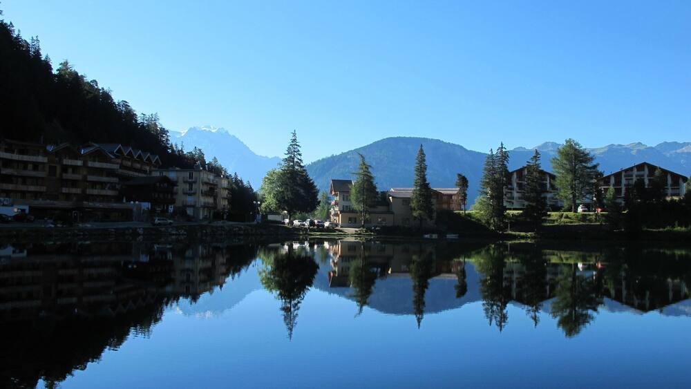 A calm lake reflecting buildings and mountains.