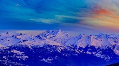 Várias montanhas cobertas de neve sob um céu colorido.