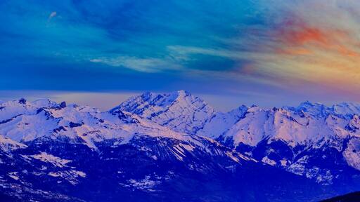 A range of snow-covered mountains under a colorful sky.