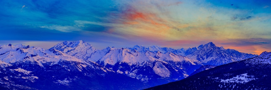 A range of snow-covered mountains under a colorful sky.