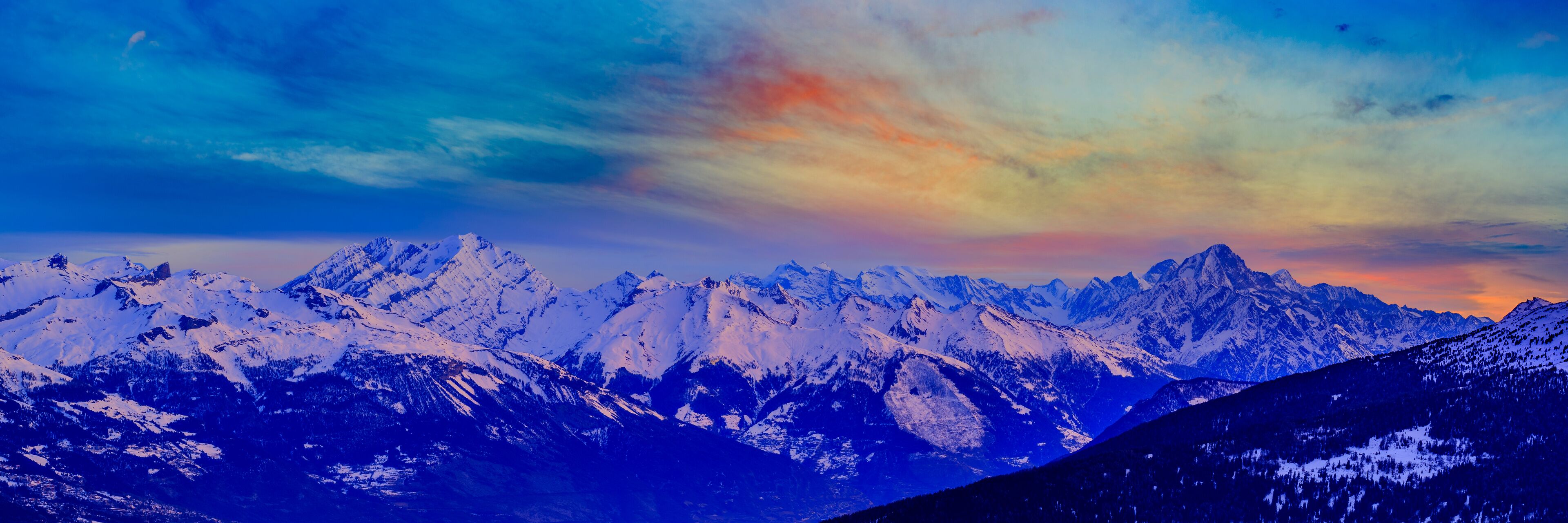 A range of snow-covered mountains under a colorful sky.