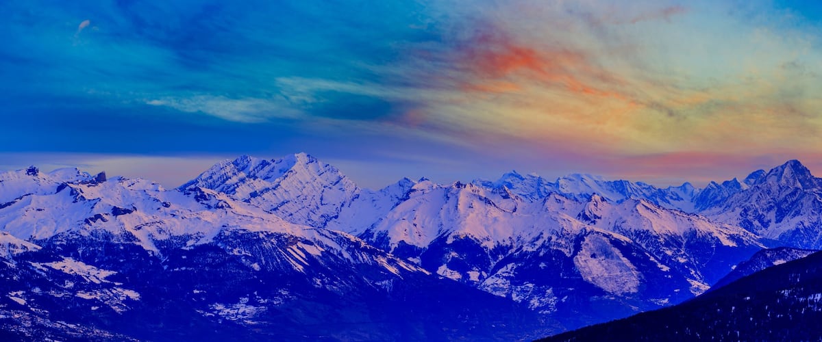 A range of snow-covered mountains under a colorful sky.