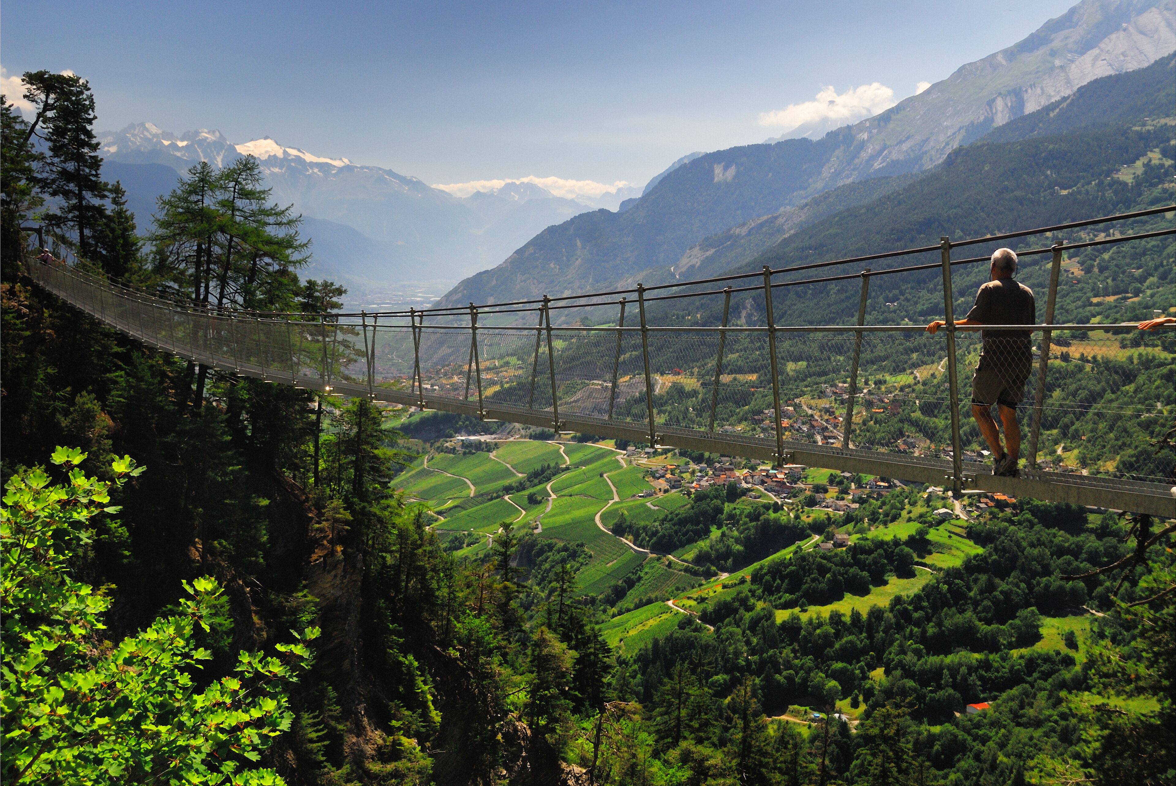 A suspension bridge over a valley with green fields and mountains in the background.