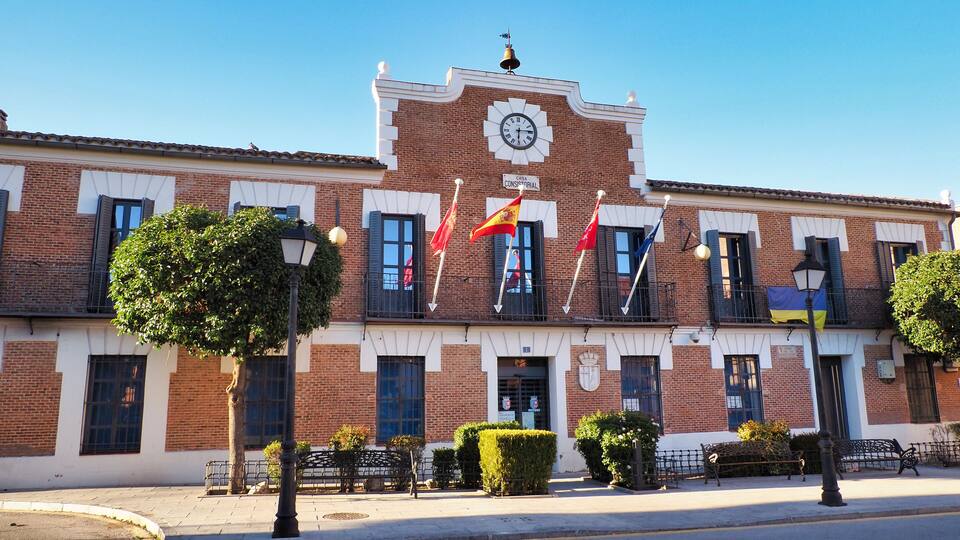 A historic building with a clock tower, red flags, and a clear blue sky.