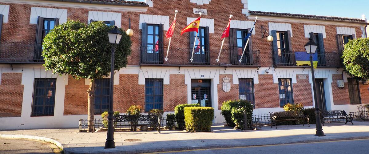 A historic building with a clock tower, red flags, and a clear blue sky.
