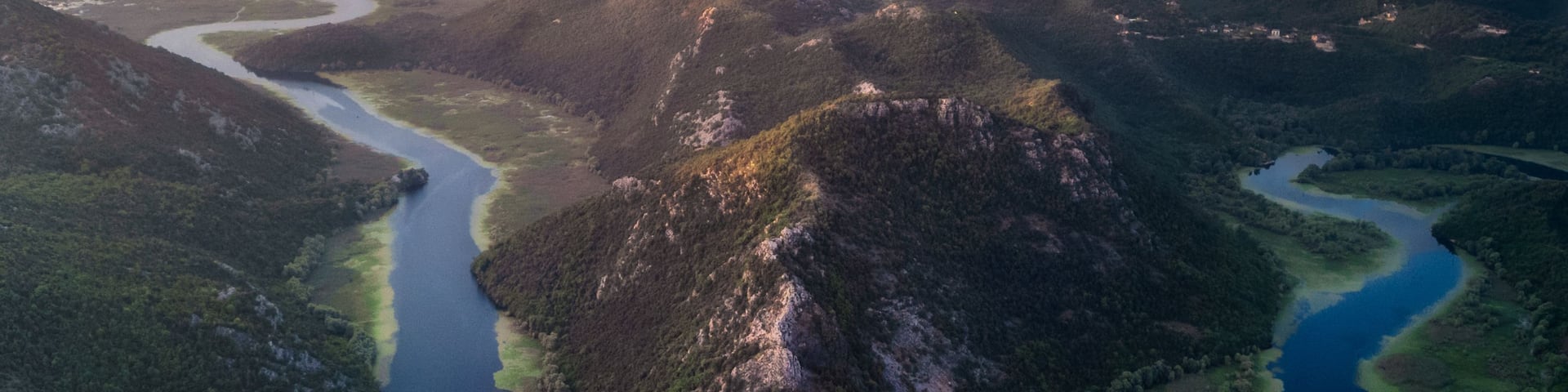 A river winding through a mountainous landscape with a forested area and a clear sky.