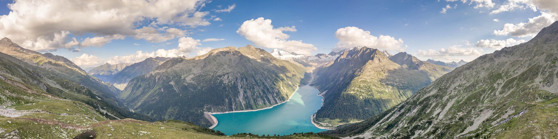 A mountainous landscape with a turquoise lake surrounded by rugged peaks and green valleys.