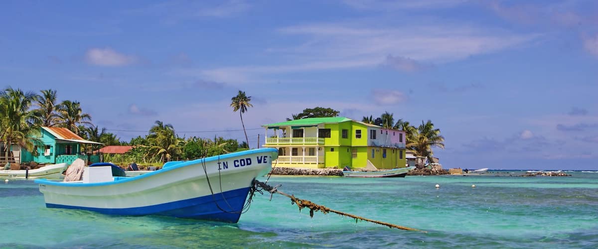 A boat named IN GOD WE TRUST anchored near a colorful house by the sea.