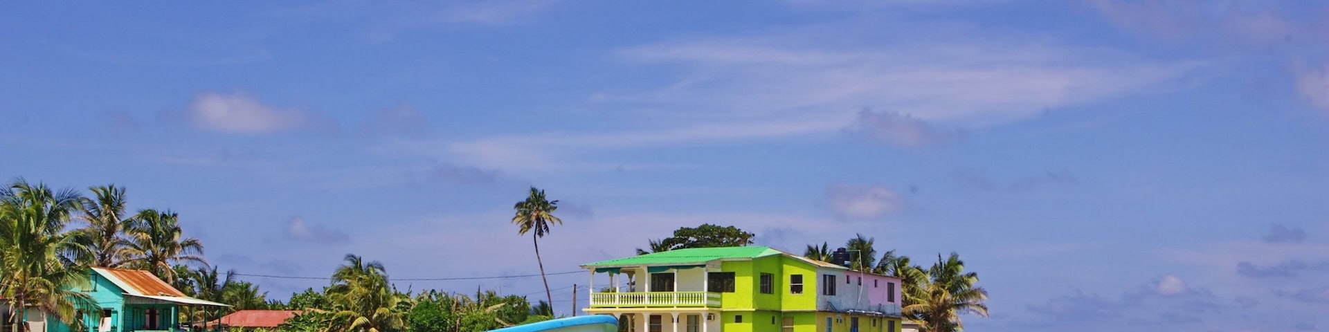 A boat named IN GOD WE TRUST anchored near a colorful house by the sea.