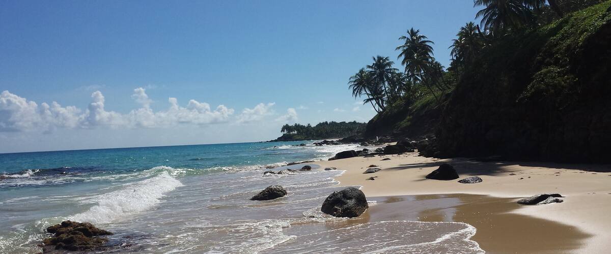 A beach with clear turquoise water, sandy shore, and scattered rocks.
