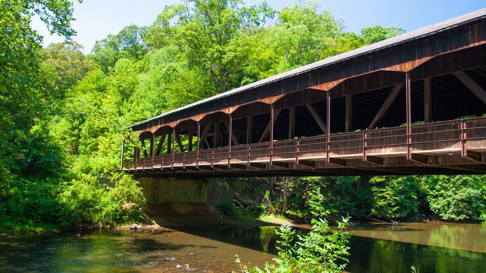A wooden covered bridge spanning a river, surrounded by lush greenery and trees.