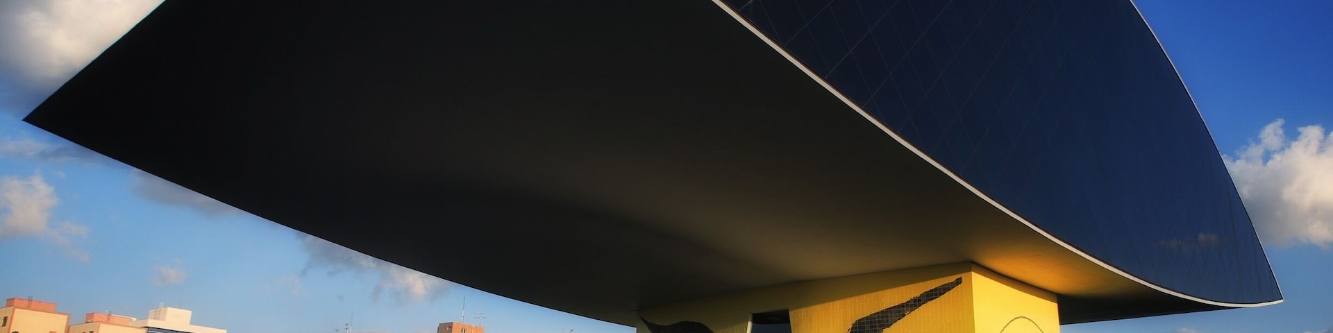 Un edificio moderno con un techo curvo grande y una base amarilla.