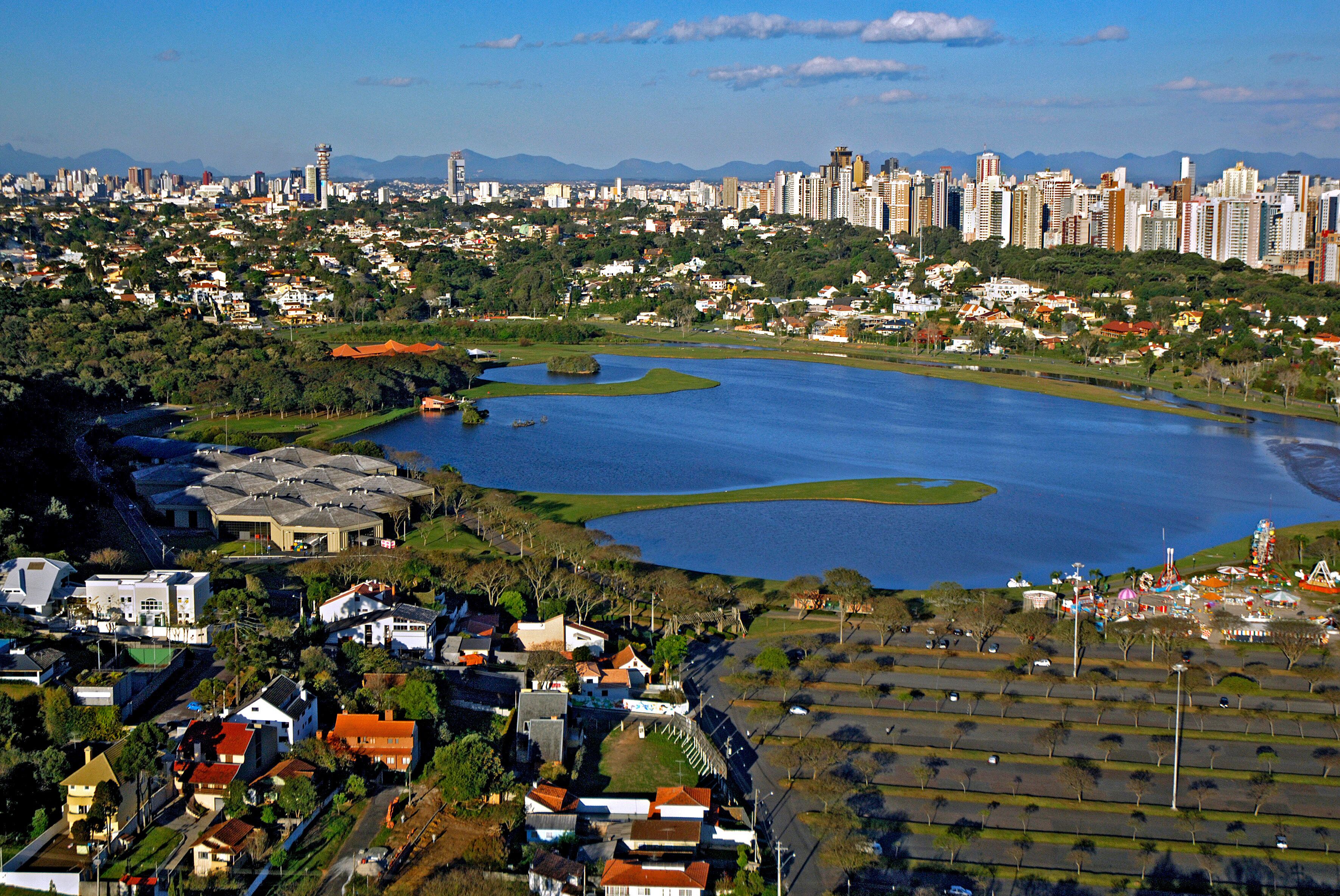 Un paisaje urbano con una gran masa de agua, zonas residenciales y montañas a lo lejos.
