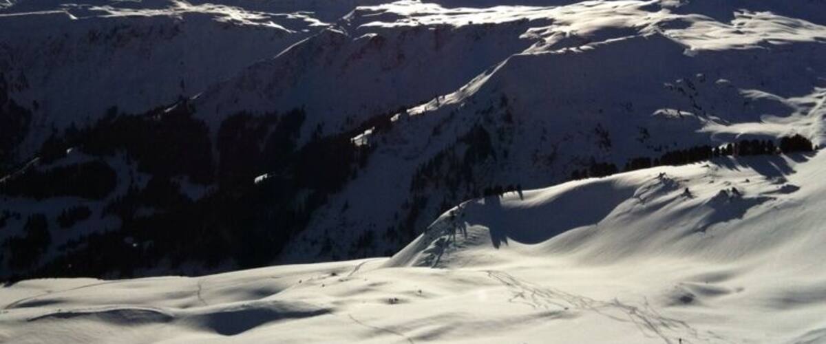 A snow-covered mountain range with the sun shining brightly in the sky.