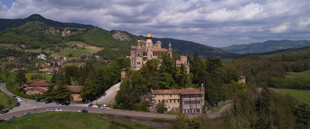 A historic castle with a golden dome, surrounded by lush green hills and a winding road.