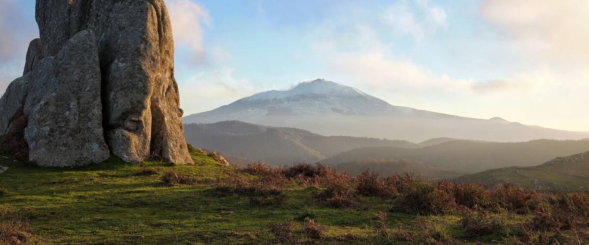 A large rock formation in a grassy field with a mountain in the background.