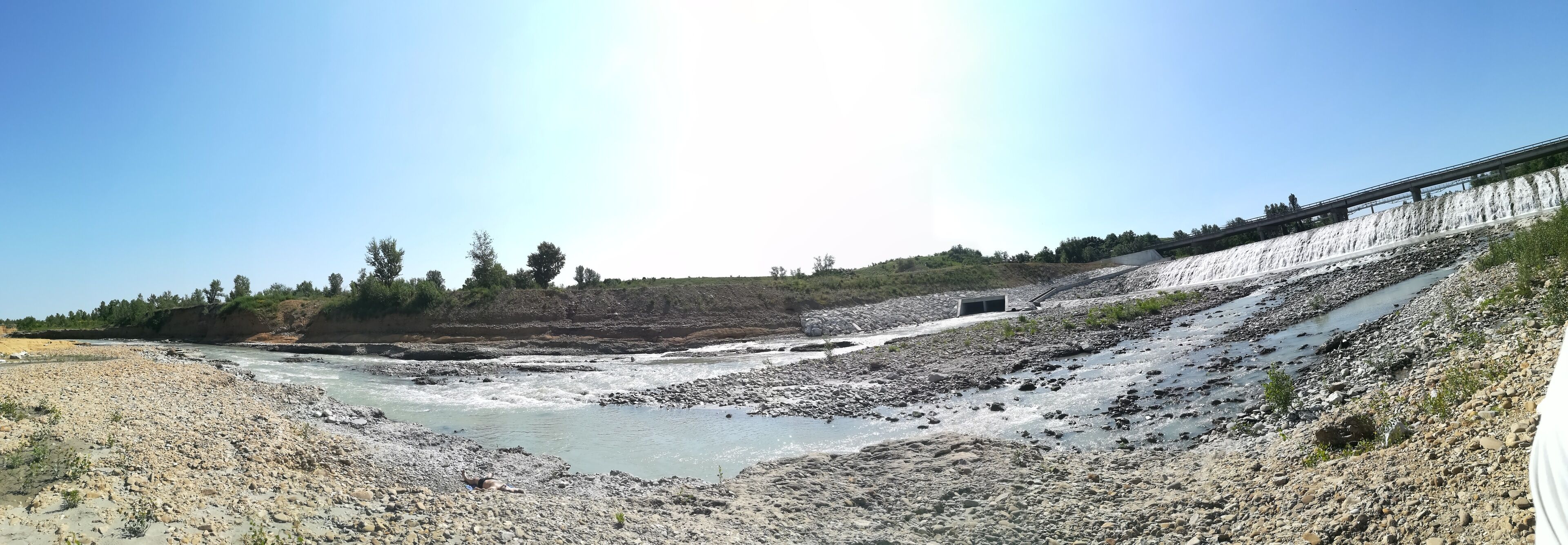 A river with a rocky bed, a bridge, and a forested hillside.
