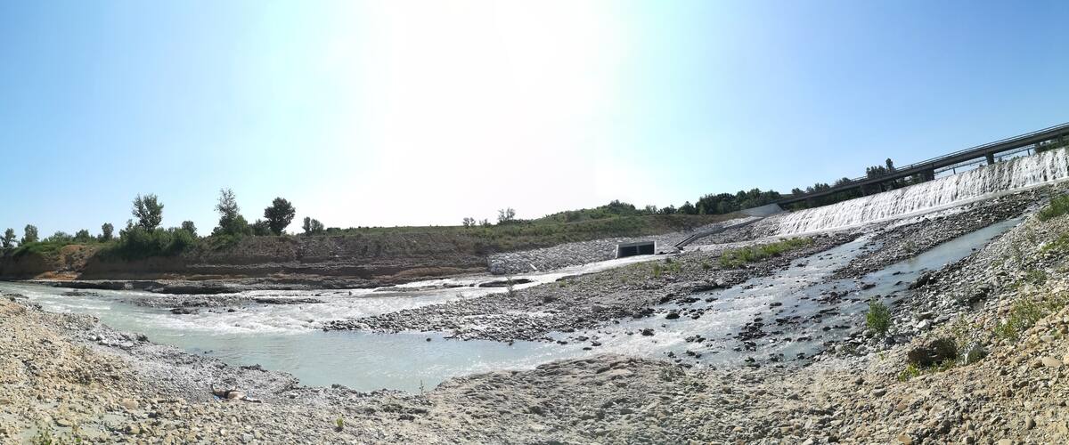 A river with a rocky bed, a bridge, and a forested hillside.