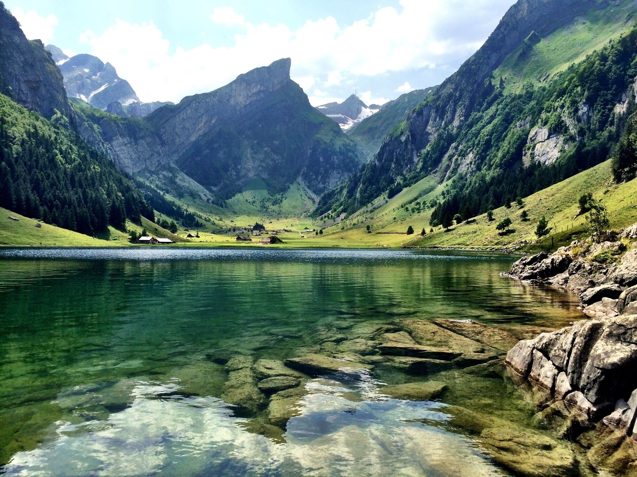 A clear mountain lake surrounded by rugged mountains and sparse vegetation.