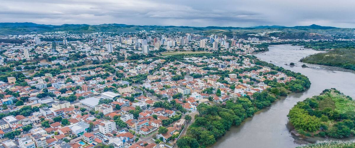An aerial view of a city with a river running through it, surrounded by greenery and hills in the background.