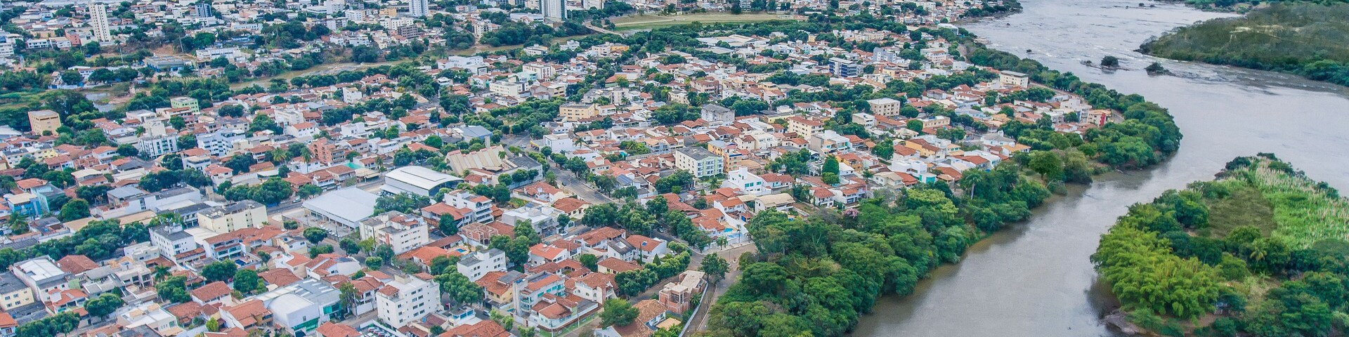 An aerial view of a city with a river running through it, surrounded by greenery and hills in the background.