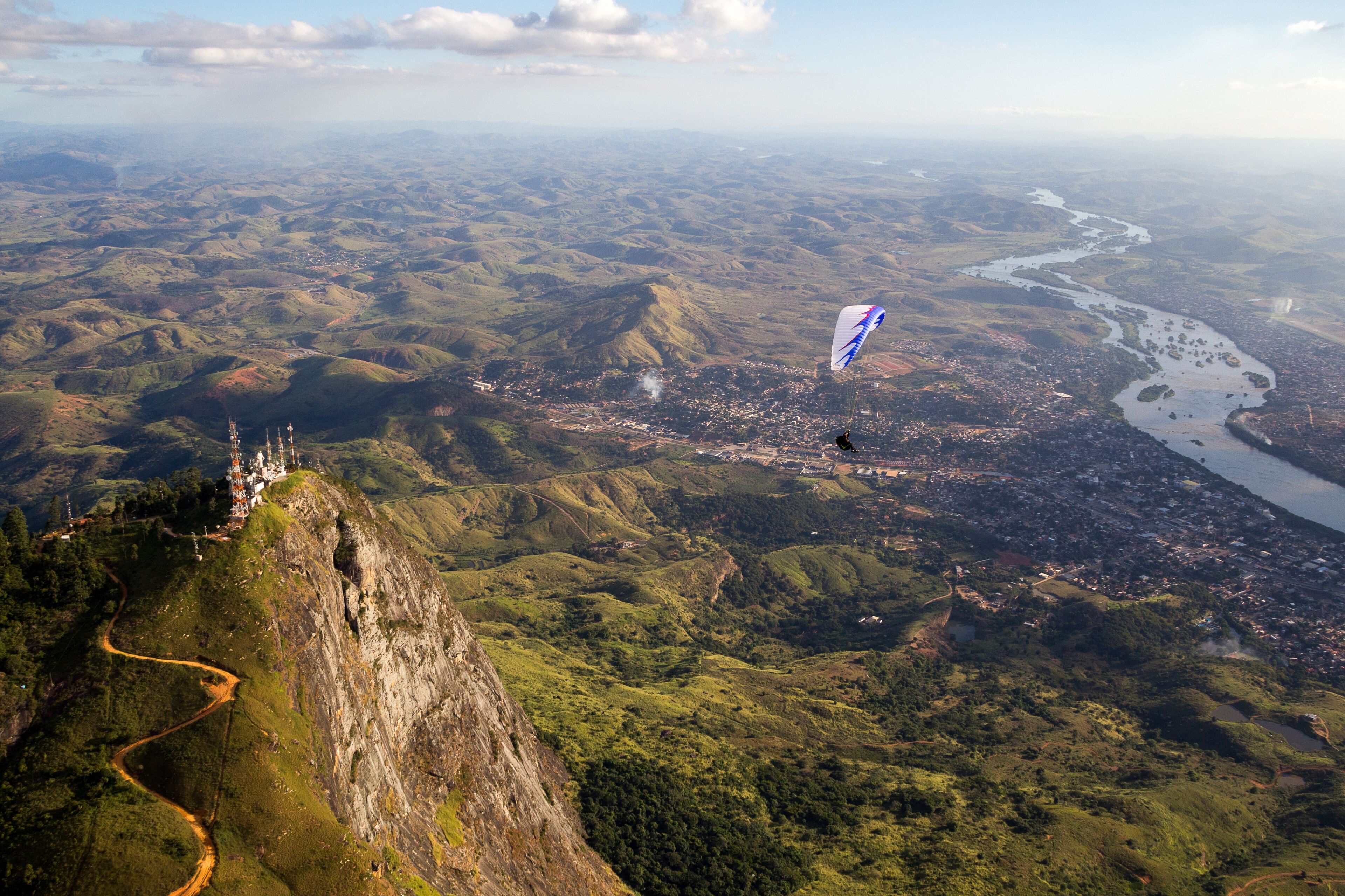 A mountainous landscape with a river, a town, and a person flying a kite.