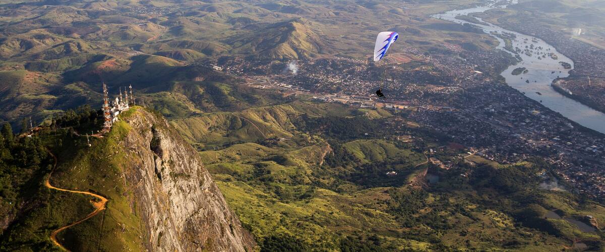 A mountainous landscape with a river, a town, and a person flying a kite.