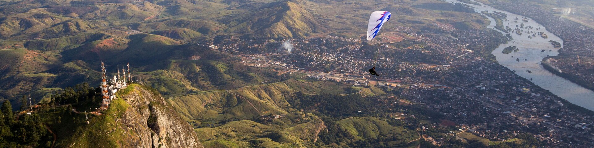 A mountainous landscape with a river, a town, and a person flying a kite.