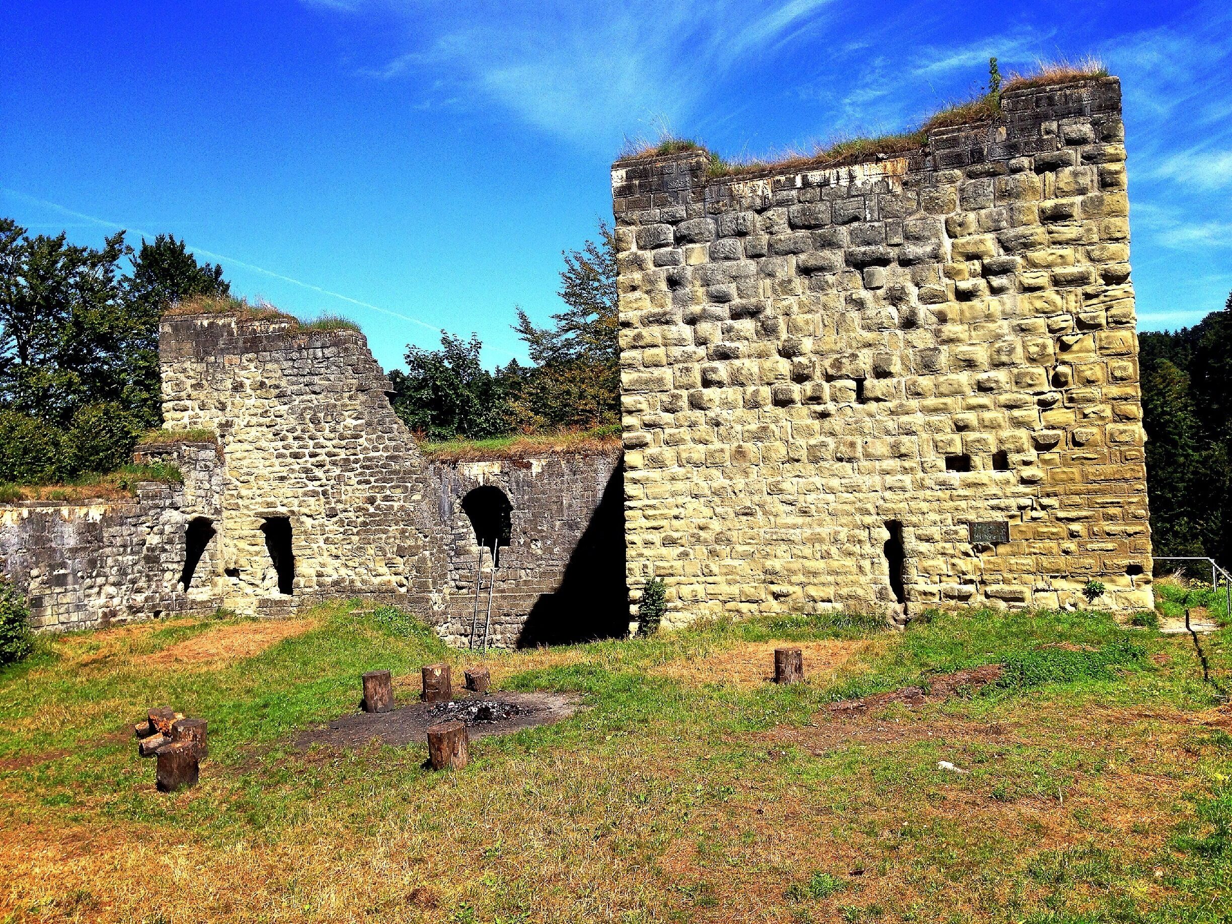 A historic stone castle ruin with arched openings and a grassy field in the foreground.