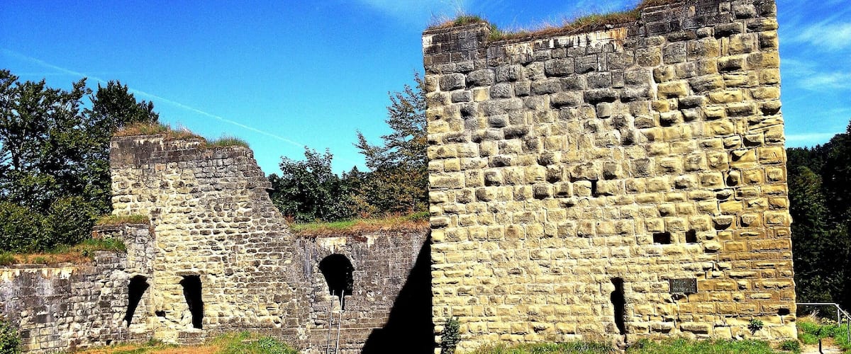A historic stone castle ruin with arched openings and a grassy field in the foreground.