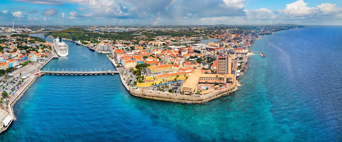 A coastal city with a prominent bridge, a large cruise ship docked, and a clear blue sea.