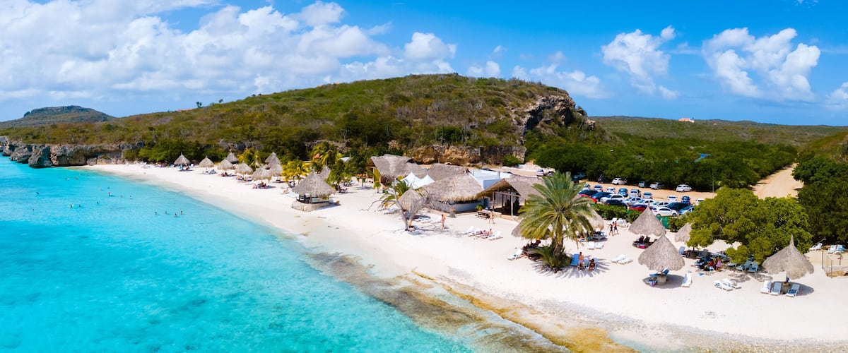 A tropical beach with clear turquoise waters, white sand, and thatched-roof huts.
