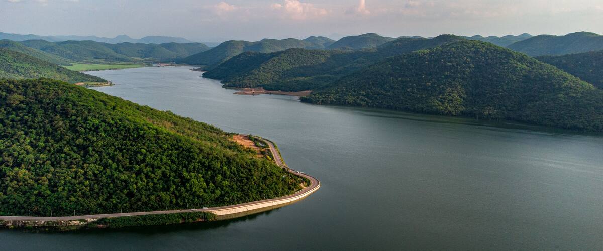 A winding road along a river, surrounded by lush green hills and mountains.