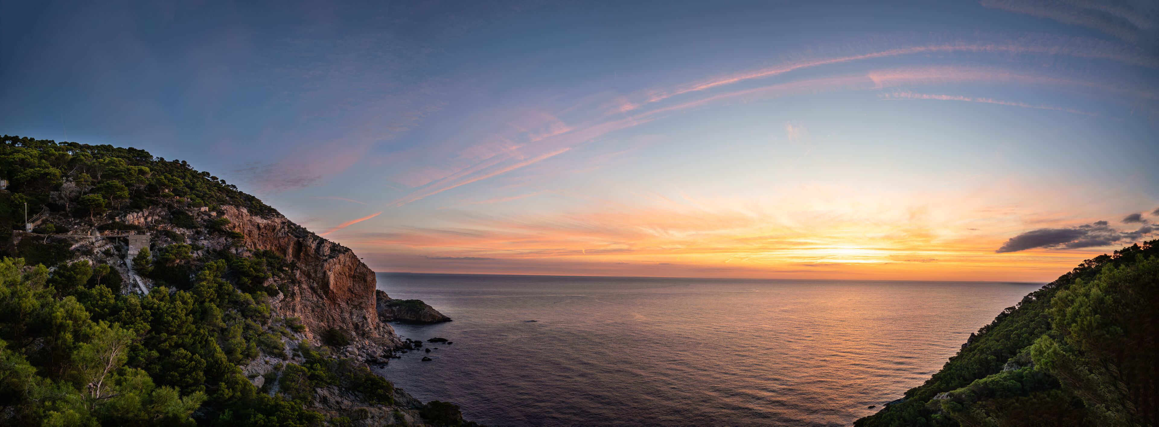 A coastal landscape with cliffs, a sunset, and calm sea.