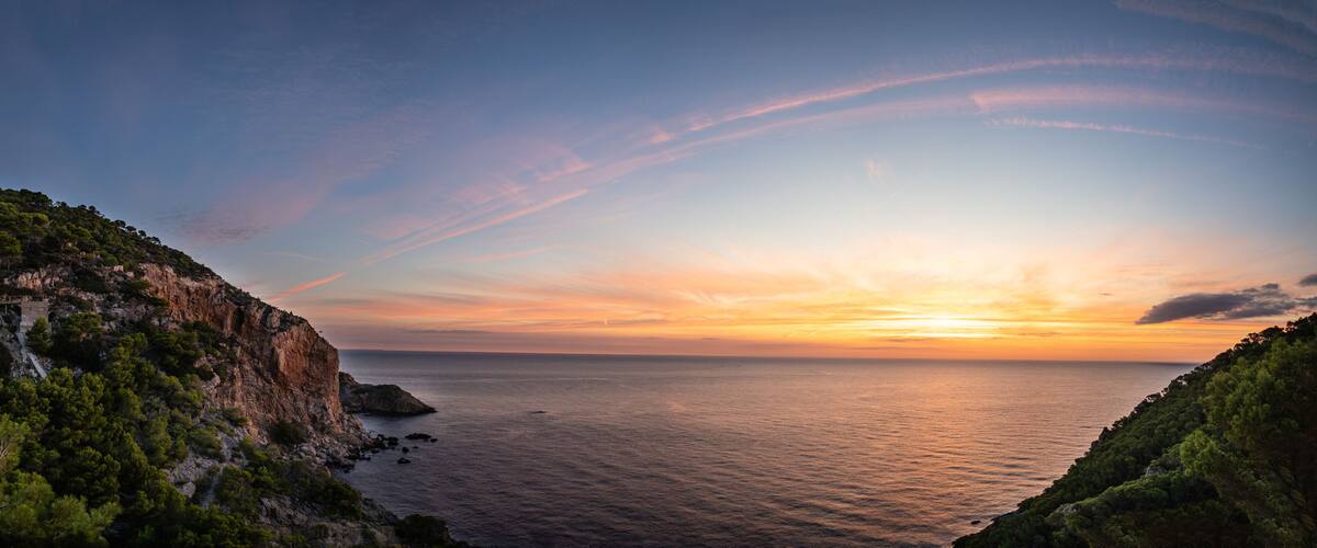A coastal landscape with cliffs, a sunset, and calm sea.
