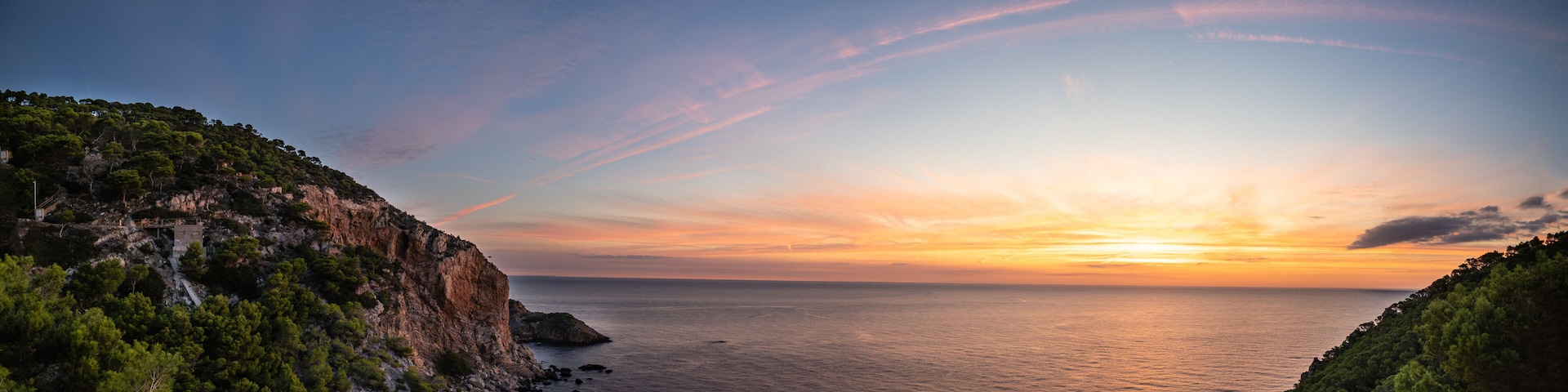 A coastal landscape with cliffs, a sunset, and calm sea.