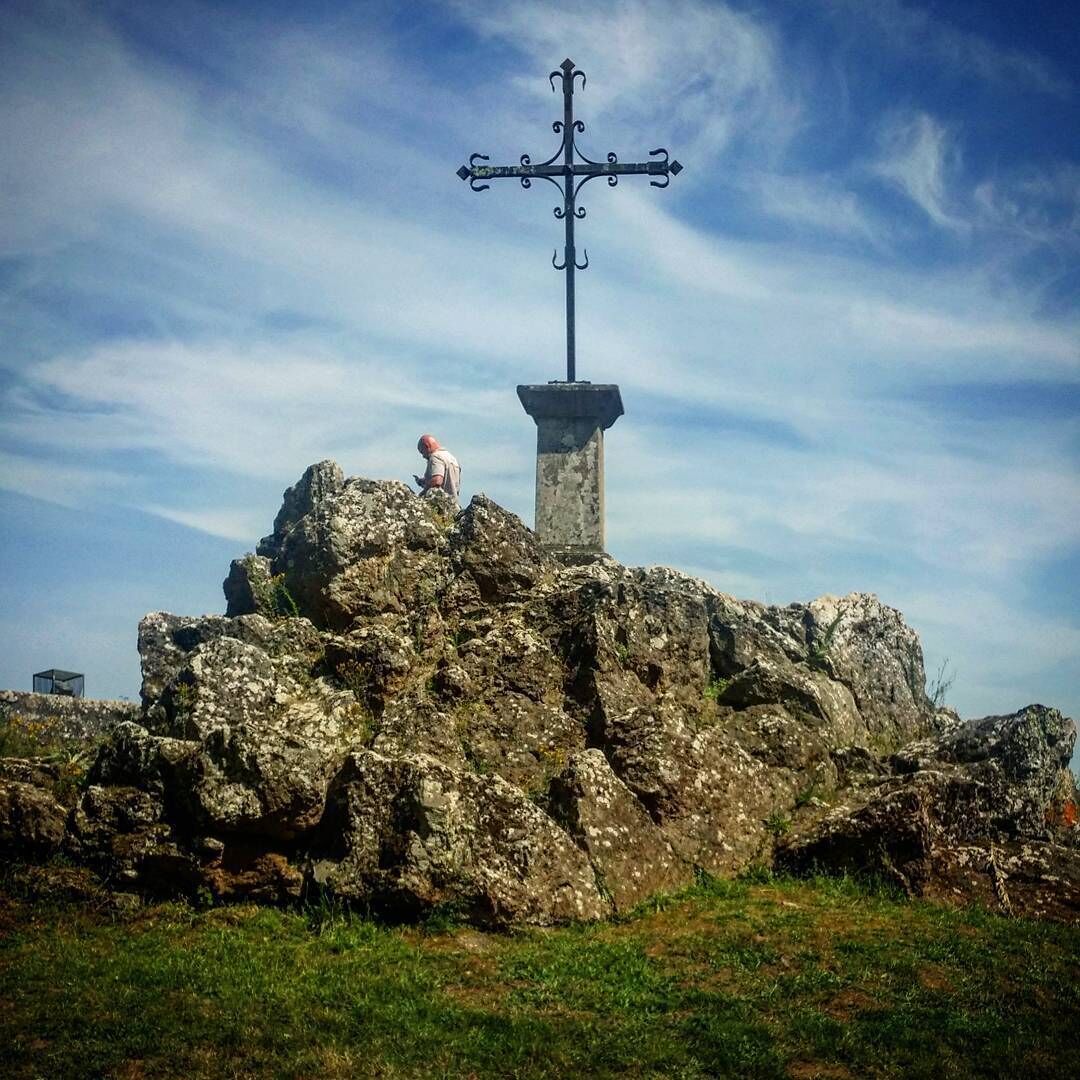 A cross on a rocky outcrop with a person standing nearby.