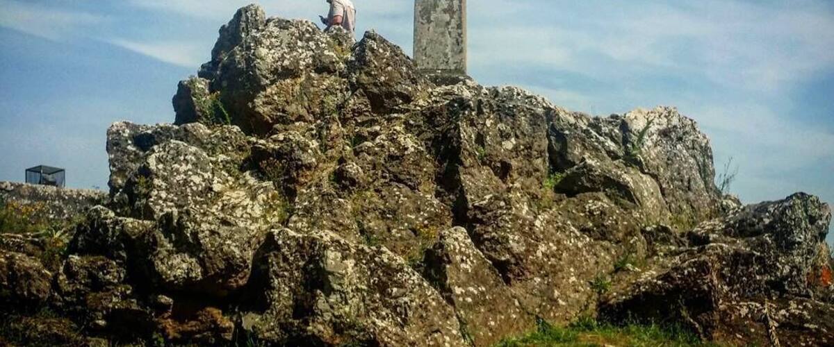 A cross on a rocky outcrop with a person standing nearby.