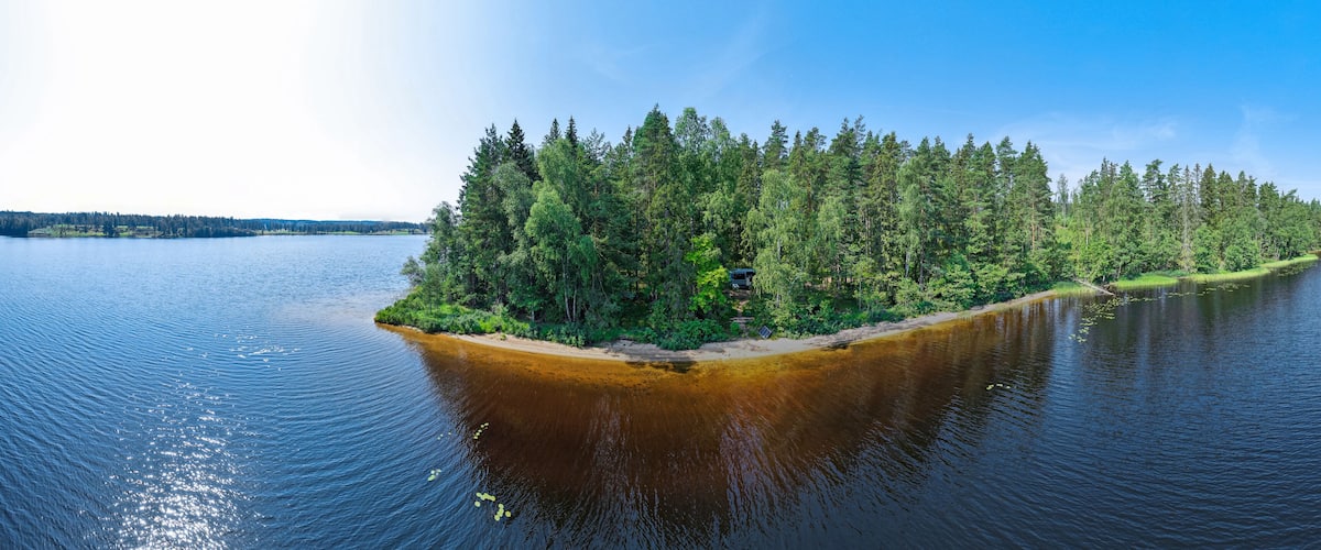 A forested island in a lake with clear water and a sandy beach.