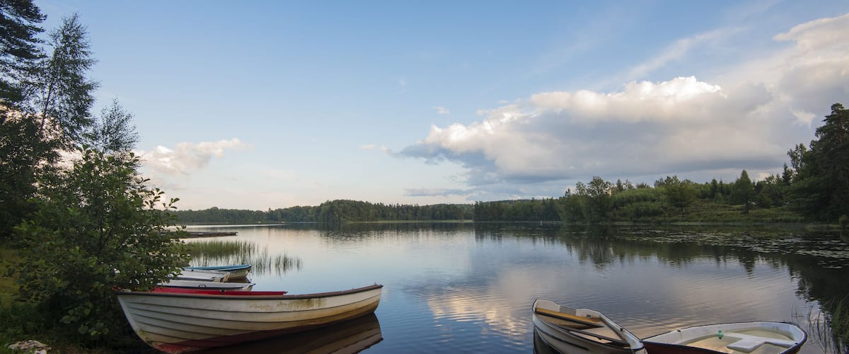 A calm lake with two boats docked at the shore, surrounded by trees and a clear sky.